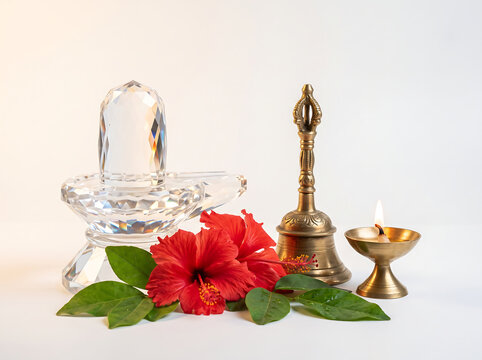 Close-up still life of a crystal Shiva Lingam with red hibiscus and brass bell on pure white background