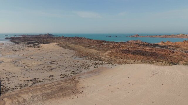 Cobo Bay Guernsey Channel Islands.Panning view of golden sandy beach and jetty out to sea over pink granite rocks towards calm sea and rocky outcrops on sunny day with clear blue sky