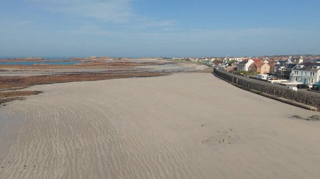Cobo Bay Guernsey Channel Islands.Forward drone footage of golden sandy beach and seafront buildings with views across rocky outcrops out to sea and horizon on bright sunny day