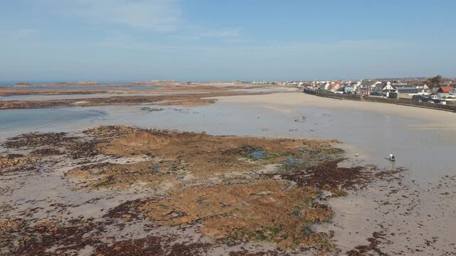 Cobo Bay Guernsey Channel Islands.Low drone footage over rocky foreshore to extensive golden sandy beach and seafront buildings with views across rocky outcrops out to horizon on bright sunny day