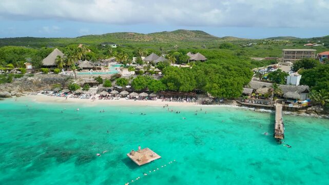 Turquoise water and white sand beach lined with thatched cabanas and relaxing tourists at Playa Kalki in Curacao