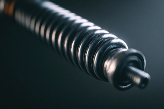 A tightly coiled spring is held in a compressed position showing energy build-up with mechanical tension against a dark background