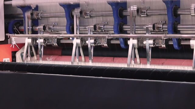 Industrial fabric slitting machine cutting black textile rolls, heavy duty textile machinery close up shot