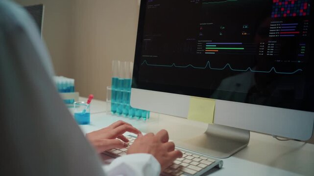 Close up of a scientist's hands typing on a computer keyboard. Medical professional working with chemical samples and analyzing data on a monitor