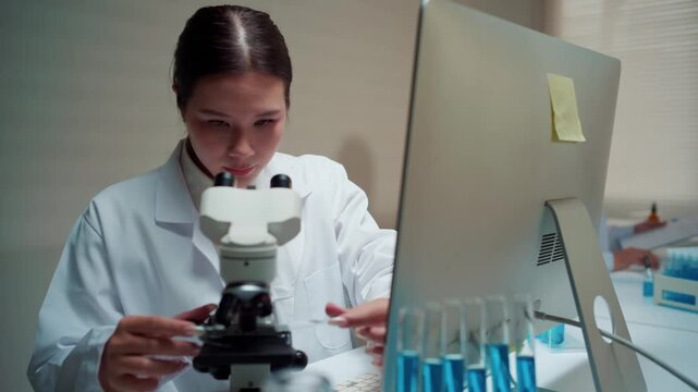 Asian female medical scientist working in a laboratory. She is placing a sample from a test tube onto a slide to analyze it with a microscope