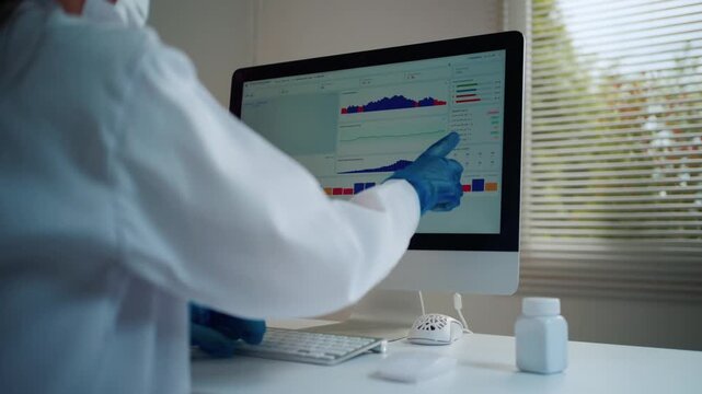 Unknown researcher wearing a lab coat and gloves working in a modern laboratory. Medical professional analyzing scientific data graphs