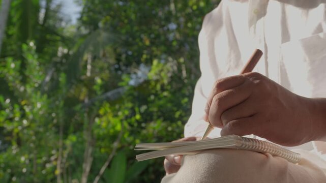 Person writing ideas in notebook outdoors, promoting mental clarity, focus, productivity, creativity, and intentional thinking