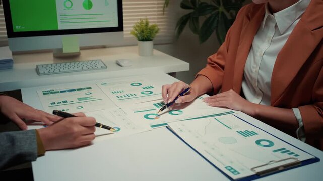 Two professional women colleagues discussing and analyzing financial reports with charts and graphs, pointing at data during a meeting
