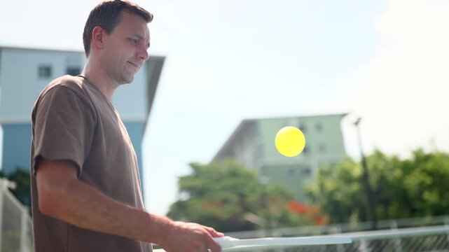 An active, athletic man, lively and cheerful, in his workout clothes, practices pickleball on the sidelines to warm up before a match. Exercise for good health.