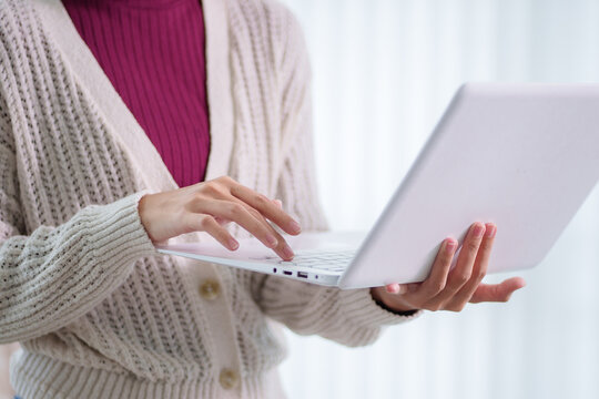 Adult woman in beige cardigan typing on white laptop computer for education and online learning with copy space
