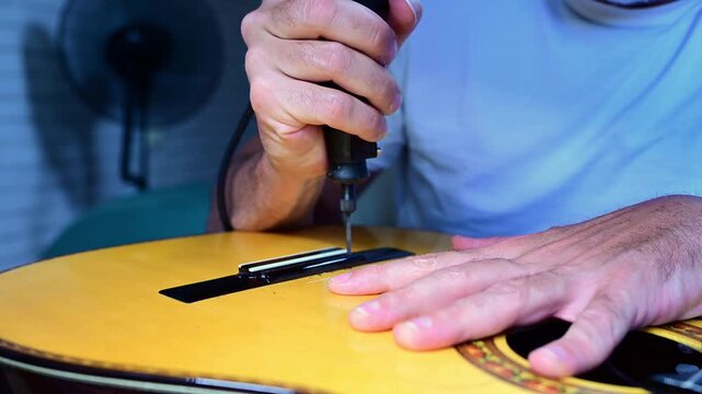 Luthier hands drilling a hole repairing an acoustic guitar bridge