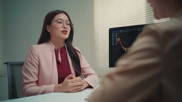 Young Asian businesswoman meeting with a client, discussing financial data on a computer screen. They talk and finalize the deal with a handshake