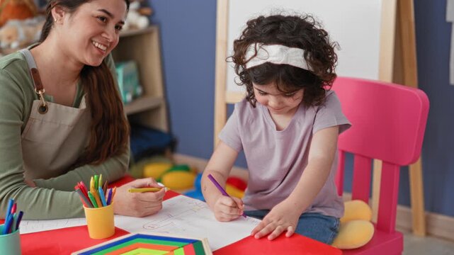 Woman teacher smiling guides girl drawing with purple pencil at red table in building; early learning joy.