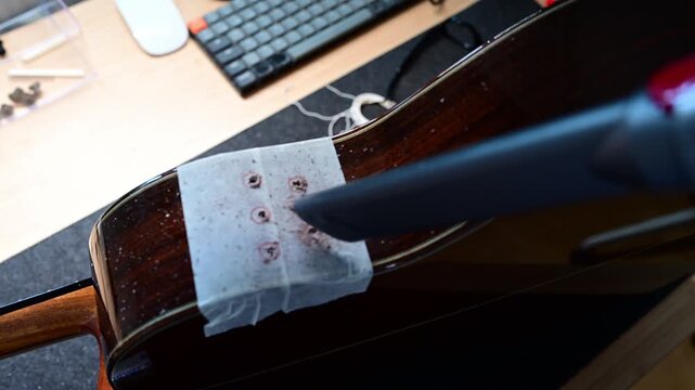 Luthier vacuuming wood dust after drilling a classic guitar