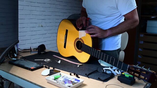 Unrecognizable luthier carefully restoring an acoustic guitar in his workshop