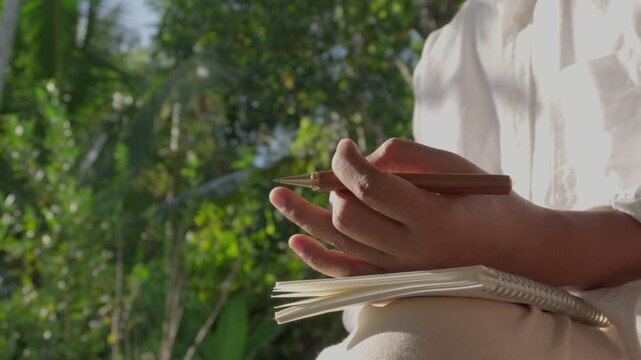 Peaceful mindful pause before creative work, Person holding pen and notebook in natural garden light, quiet reflection for mental clarity, stress relief, focus improvement, creativity and inspiration