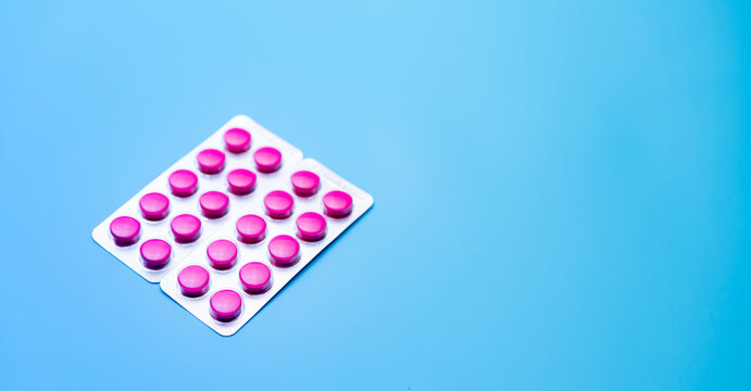 Round pink tablets pills in blister pack on blue background with space for text. Painkiller medicine. Online pharmacy and pharmacy web banner. Migraine headache and menstrual pain treatment pills.