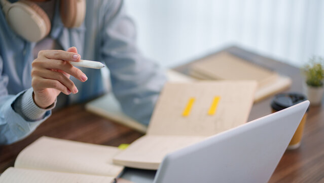 Adult student holding pen while studying with notebook and laptop at wooden desk during online learning session
