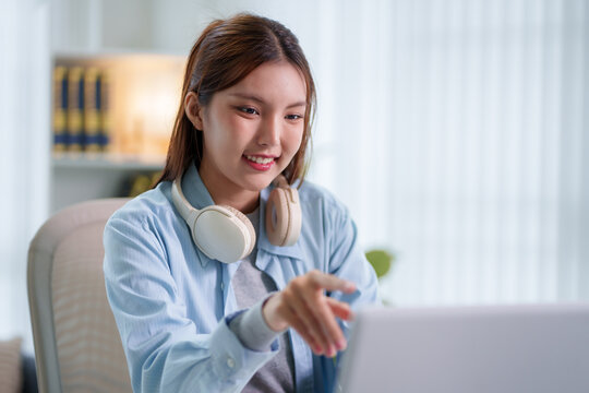 Young Asian woman student with headphones gesturing during online video call on laptop at home with copy space