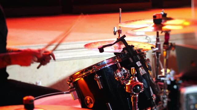 Close-up of drummer performing on drum kit under colorful stage lights. Live concert, percussion instrument, music performance and entertainment event.