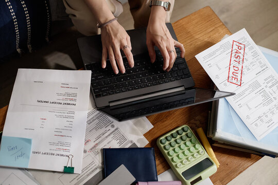 Overhead shot of young adult woman typing on laptop while reviewing past due bills, budgeting expenses and managing debt. Ideal for personal finance, late payment or debt relief marketing