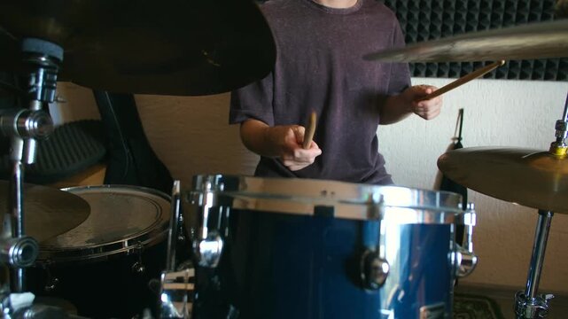 Young man holding drumsticks playing rhythm on acoustic drum kit. Musician practicing in soundproof room, hitting hi hat and high tom drum. Drummer playing beat on blue drum kit in recording studio