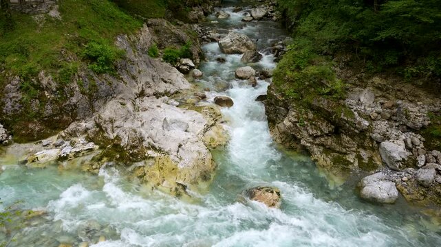 The clear turquoise waters of the Tolminka and Zadla&scaron;čica rivers merge and flow gently through rocky terrain surrounded by lush green forest in Slovenia&rsquo;s Triglav National Park.