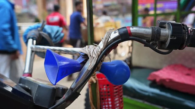 A close-up detail shot captures a blue squeeze horn tied to a traditional rickshaw handlebar in Dhaka. Ideal b-roll for classic transit machinery, street transport parts, and urban sound symbols.