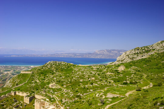 A panoramic view of the ancient ruins of Acrocorinth, Greece, overlooking the Gulf of Corinth on a clear day.