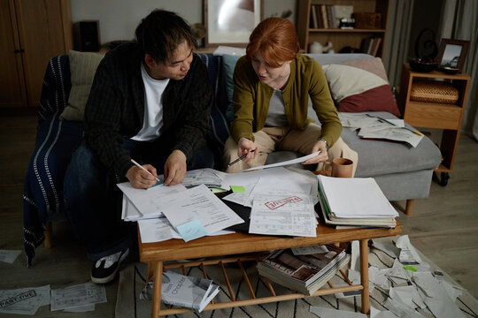 Young adult couple reviewing bills and signing paperwork at home, managing household budget and debt. Image supporting personal finance, loan stress, insurance or tax content