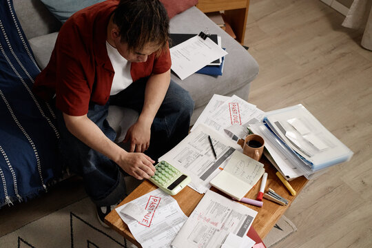 High angle shot of man calculating overdue bills, managing household budget and debt stress. Useful for finance content