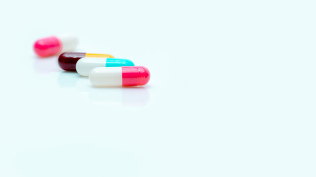 Selective focus on antibiotic capsule pill. Pharmaceutical industry. Prescription drugs. Pharmacy web banner. Pink, blue, yellow, red capsules pill on white background. Antibiotic drug resistance.