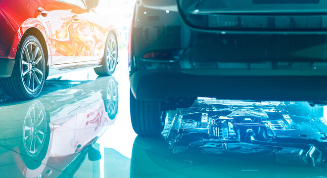 Closeup chassis, shaft, muffler of car reflected on shiny floor of showroom. New luxury car parked in modern showroom. Auto leasing business. Car dealership office. Machine and motor under the car.