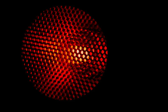 Closeup honeycomb grid texture with red light. Red and dark metal hexagon shaped pattern abstract background. Light modifier equipment. Metal honeycomb. Futuristic pattern. Honey grid cells network.