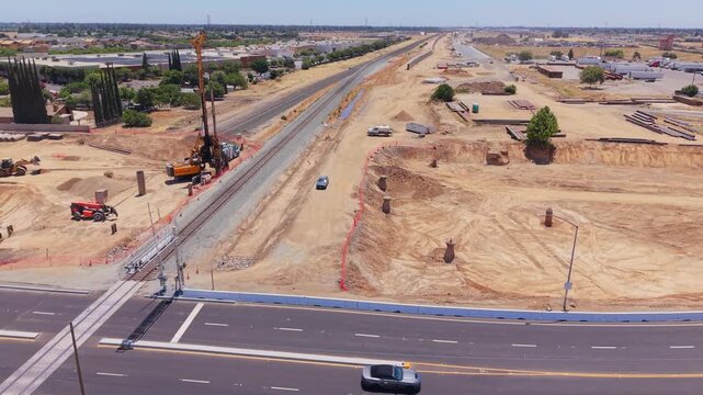Ascending Aerial Drone Shot Over California High Speed Rail Construction With Railroad Crossing Foundation Drill Tractor Moving Dirt and Traffic
