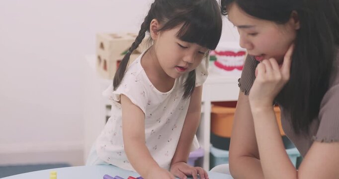 Smart Asian little girl sorting colorful wooden pegs on board with her mother.