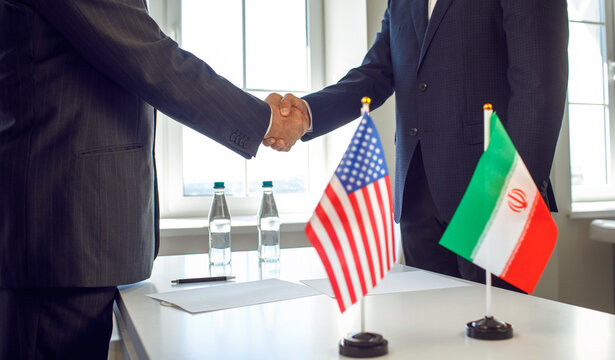 Handshake diplomacy agreement negotiation treaty by diplomats. USA and Iran flags stand by documents during cordial meeting. Symbolizes international politics diplomacy and bilateral agreement.