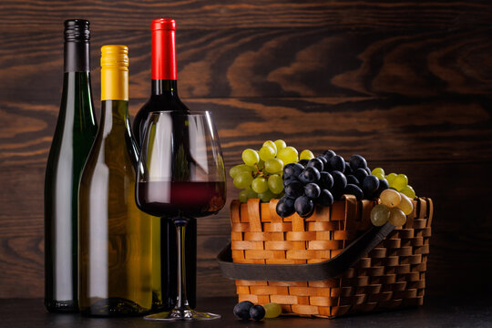 Red and white wine bottles with a glass and basket of fresh grapes