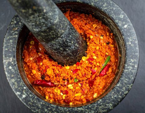 Grinding red chilies and spices in a stone mortar for authentic Thai red curry paste.