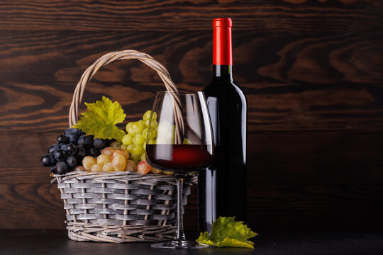 Red wine bottle with a glass and basket of fresh grapes