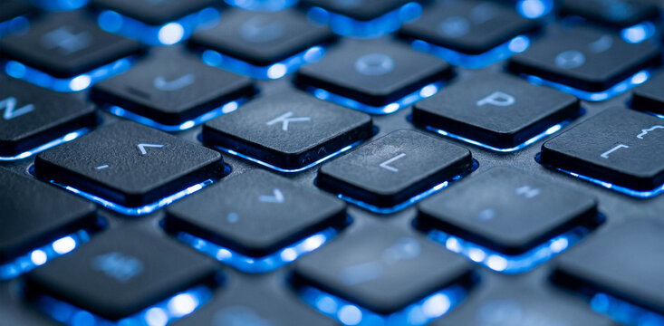 Close-up view of a modern computer keyboard with illuminated keys, showcasing the letters and symbols in a dynamic and high-tech setting.