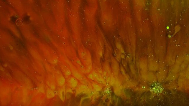 Visceral macro video capturing red and orange fluid textures intermingling with shimmering green micro-bubbles, forming unique organic abstract patterns.