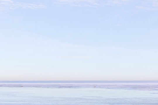 A tranquil, minimalist winter landscape showing a vast frozen sea under a soft pale blue sky. Quiet, cold and expansive mood with subtle ice texture and distant shoreline in blue pink hues