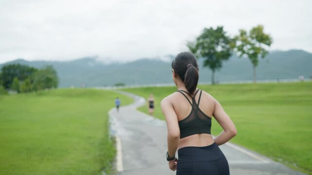 Young female runner checking her smartwatch before running in the park, representing fitness tracking, digital health, active lifestyle, preventive care, longevity and health insurance concept.