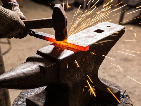 A close-up of a blacksmith shaping hot glowing metal on an anvil with sparks flying everywhere.