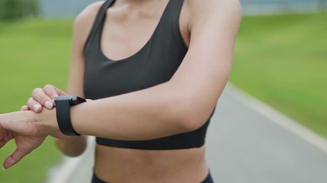 Woman adjusting a smartwatch before starting a run on an outdoor track in a public park, representing fitness preparation, wearable technology, healthy lifestyle and preventive health concept.