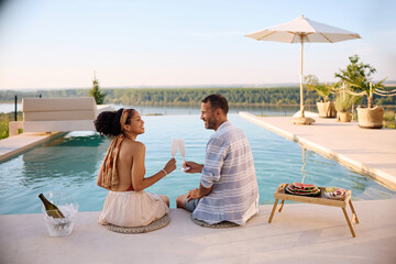Fototapeta na wymiar Carefree couple toasting with champagne while relaxing by the infinity pool on summer vacation.