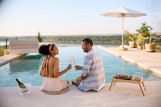 Carefree couple toasting with champagne while relaxing by the infinity pool on summer vacation.