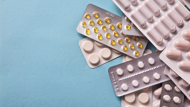 Flat lay of assorted medical pills in blister packs, pharmaceutical tablets heap on blue background with copy space