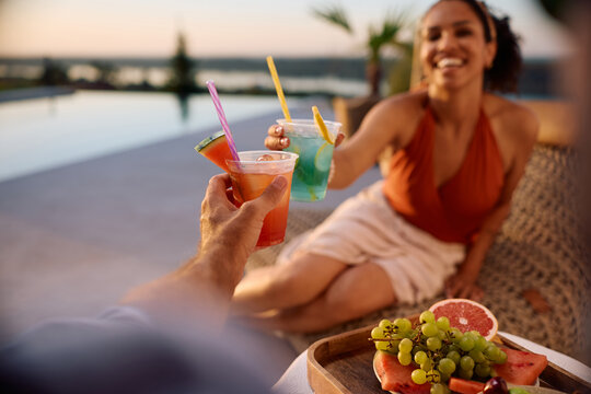 Close up of couple toasting with cocktails at summer sunset.